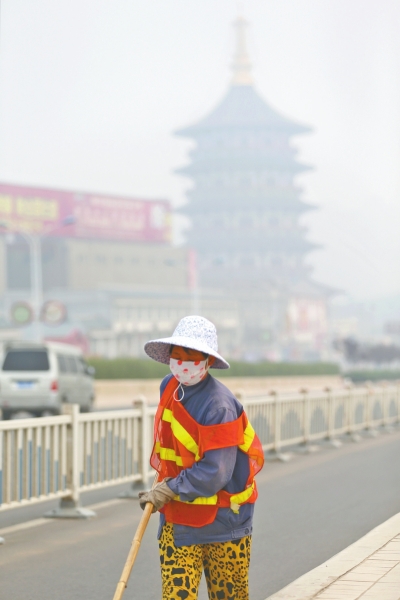 近日，在古都洛陽(yáng)，環(huán)衛(wèi)工人身后的“天堂”被霧霾籠罩著。