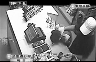 戴帽男子一手掐住加油站營(yíng)業(yè)員，一手持發(fā)令槍指向另一營(yíng)業(yè)員，要求“把錢給我裝起來”。