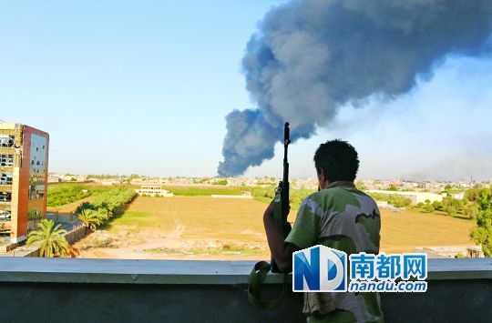 2日，利比亞首都的黎波里，一民兵武裝成員眺望被火箭彈擊中的儲油罐冒出濃煙。