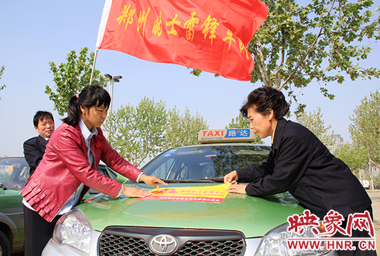 　　授旗結(jié)束后，首都的士雷鋒車隊王鳳進隊長（右）與鄭州的的哥的姐在車身上貼上標識。