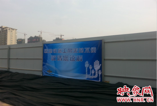 道路南側(cè)圍起了白色的圍擋，墻上標(biāo)示著“因地鐵施工帶來(lái)的不便敬請(qǐng)您諒解”的提示牌。