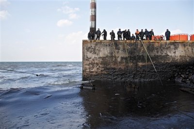 昨日，山東青島，清污人員正在海邊清理油污。