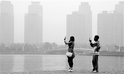 29日中午，鄭東新區(qū)如意湖畔，兩個年輕人拍攝霧霾中的景色。 鄭州晚報記者 馬健 圖