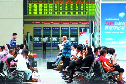 候車(chē)大廳溫度很高，一名乘客一手扇風(fēng)、一手擦汗