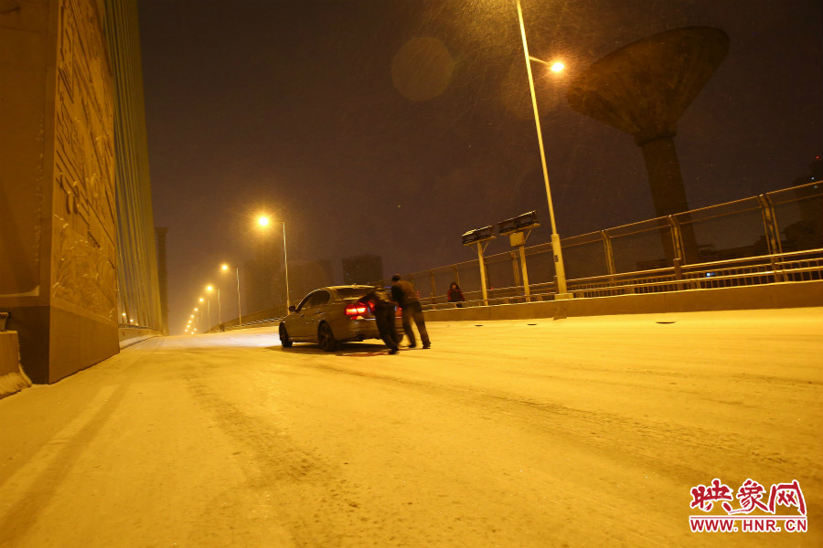 雪天路滑，汽車上橋打滑，兩名“推車人”幫助一輛私家車上坡。