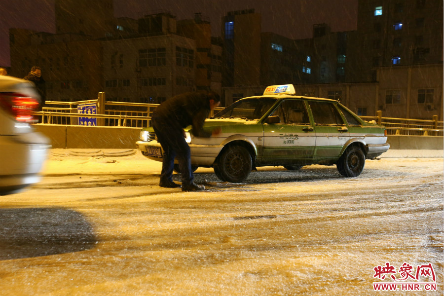 一位出租車司機在車輪前灑上雪，希望能增加輪胎的摩擦力。