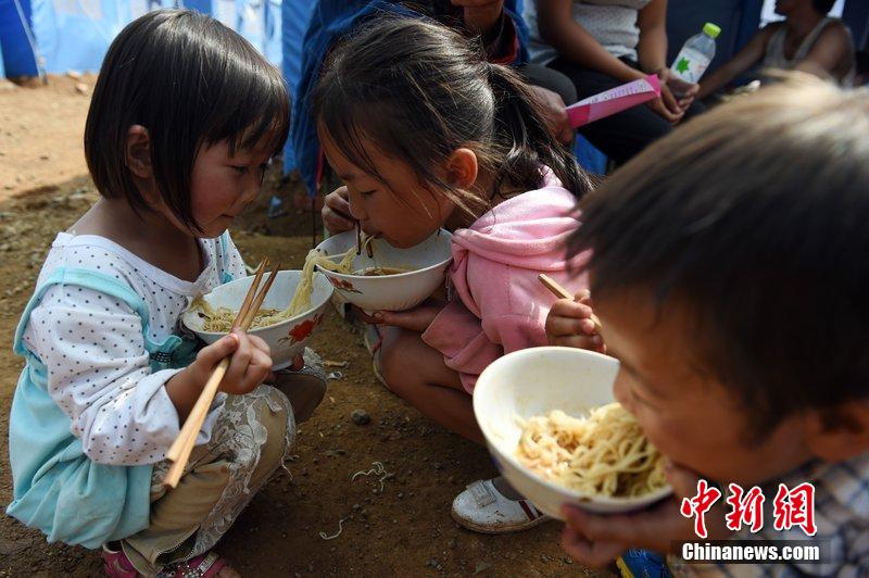 2014年8月6日，云南魯?shù)辇堫^山災(zāi)區(qū)，兒童在帳篷外吃飯。