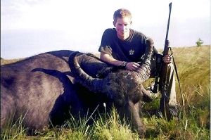 哈里王子手持獵槍，蹲在一頭遭到獵殺的水牛旁邊