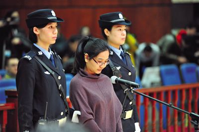 被告人盧梅低著頭，站在朝陽(yáng)法院刑事審判庭的被告席上。