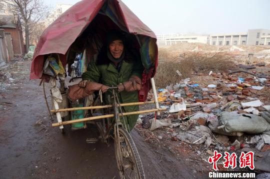 圖為老人走出窩棚，推著三輪車準(zhǔn)備出去撿拾廢品。周小云 攝